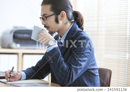 一位戴著眼鏡的商人正在辦公桌前工作。 141591136