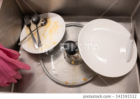 Top view of dirty dishes, plates, cutlery and a glass piled inside a stainless steel kitchen sink, showing washing up, household chores and everyday kitchen cleaning routine daily Top view of dirty dishes, plates, cutlery and a glass piled inside a stainless steel kitchen sink, showing washing up, household chores and everyday kitchen cleaning routine daily 141591512