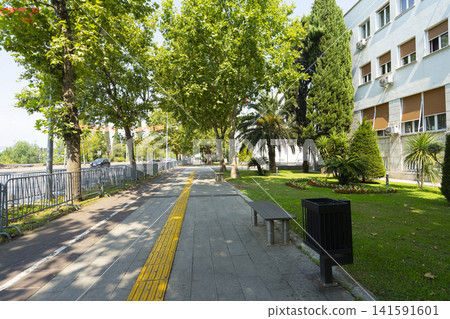 A paved sidewalk with a yellow tactile paving strip runs alongside in Podgorica, Montenegro A paved sidewalk with a yellow tactile paving strip runs alongside in Podgorica, Montenegro 141591601