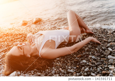 Woman beach swimsuit relaxing on a pebble shore by the sea at sunset during a summer vacation holiday Woman beach swimsuit relaxing on a pebble shore by the sea at sunset during a summer vacation holiday 141591711