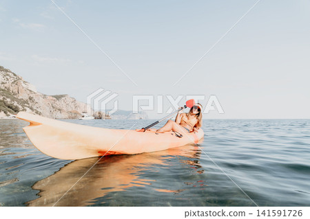 Kayaking Sea Coastline Paddleboarding Adventure - Woman paddling in a kayak on the sea near a coastline. Kayaking Sea Coastline Paddleboarding Adventure - Woman paddling in a kayak on the sea near a coastline. 141591726