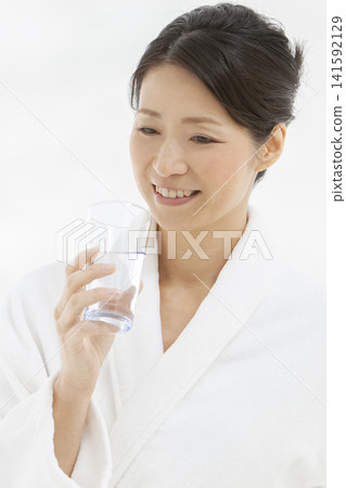 一位中年婦女穿著浴袍喝水。 141592129