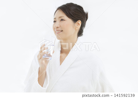 一位中年婦女穿著浴袍喝水。 141592139