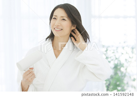 A middle-aged woman drying her hair while wearing a bathrobe. A middle-aged woman drying her hair while wearing a bathrobe. 141592148