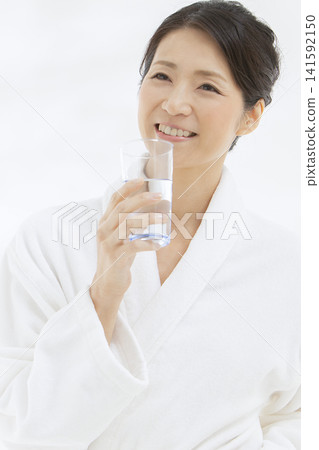 一位中年婦女穿著浴袍喝水。 141592150
