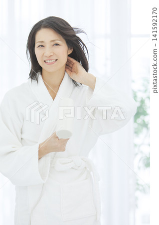 A middle-aged woman drying her hair while wearing a bathrobe. A middle-aged woman drying her hair while wearing a bathrobe. 141592170