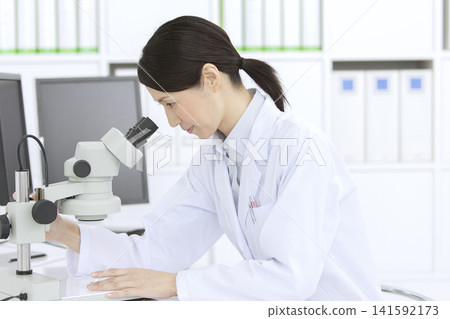A woman in a white coat looking through a microscope A woman in a white coat looking through a microscope 141592173