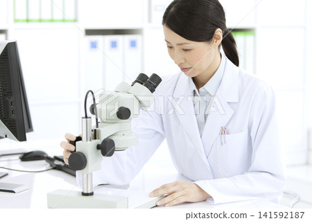 A woman in a white coat looking through a microscope A woman in a white coat looking through a microscope 141592187