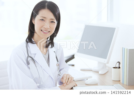 一位身穿白大褂的女醫生坐在桌前。 141592214
