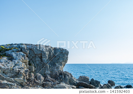 A majestic rock face rising against the blue sky and blue sea. A majestic rock face rising against the blue sky and blue sea. 141592403