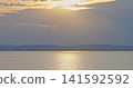 Sun setting over calm lake water and distant mountains 141592592