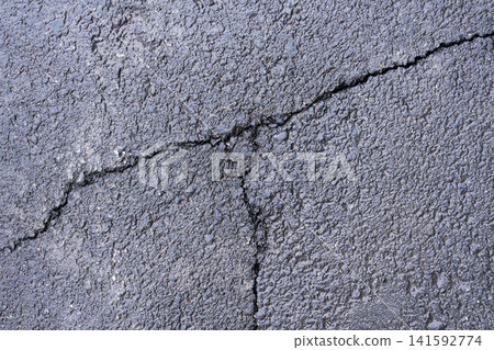 A street in a city displays cracked asphalt with rough texture and visible wear A street in a city displays cracked asphalt with rough texture and visible wear 141592774