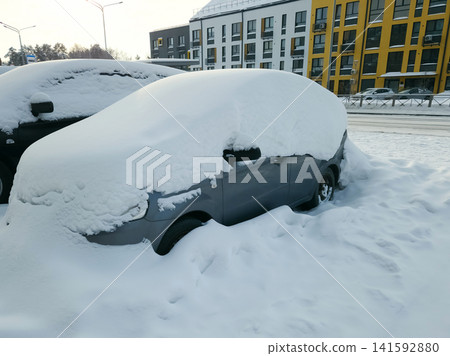 A parked car is buried in snow early in the day. Other vehicles are nearby in a residential area A parked car is buried in snow early in the day. Other vehicles are nearby in a residential area 141592880