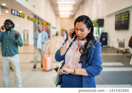 Businesswoman talking on phone checking time in airport Businesswoman talking on phone checking time in airport 141592988