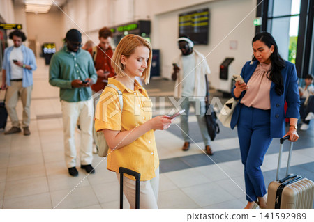 People waiting in line at airport terminal using smartphones People waiting in line at airport terminal using smartphones 141592989