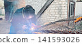 Welder wearing mask, goggles and hardhat sparks and smoke while fabricating steel on a construction site workshop, showcasing industrial safety gear, skill and heavy-industry metalwork. 141593026