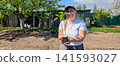 Happy woman holding a young green plant in a pot with soil, preparing to plant it in her home garden on a sunny spring day, embracing sustainability and growth. 141593027