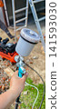 Worker hand holding a professional paint sprayer gun with an air compressor and ladder in the blurred background, preparing for home renovation or diy project. 141593030