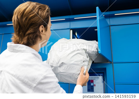 Man picking up a package from a blue parcel locker. Contactless delivery, ecommerce logistics, and self-service terminal technology for convenient online shopping. 141593159