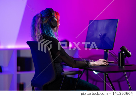 Young woman gaming at computer in vibrant purple and blue studio Young woman gaming at computer in vibrant purple and blue studio 141593604
