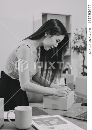 Startup SME small business entrepreneur of freelance Asian woman wearing apron using laptop and box to receive and review orders online to prepare to pack sell to customers, online sme business ideas. Startup SME small business entrepreneur of freelance Asian woman wearing apron using laptop and box to receive and review orders online to prepare to pack sell to customers, online sme business ideas. 141593665