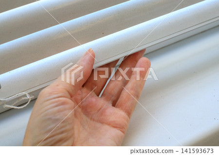 Woman's hand touches dusty white blinds. Dusting blinds indoors, cleaning. 141593673