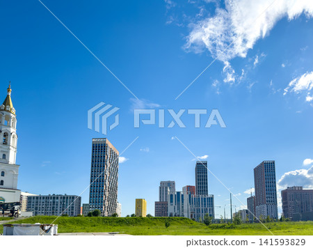 Modern skyline featuring a mix of residential buildings and a church, set against a clear blue sky. The landscape includes green grass and a well-maintained urban environment Modern skyline featuring a mix of residential buildings and a church, set against a clear blue sky. The landscape includes green grass and a well-maintained urban environment 141593829