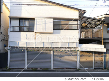 一幅展現日本老式商店兼住宅全景的畫面，其特色在於遮陽篷框架和百葉窗。 141594020