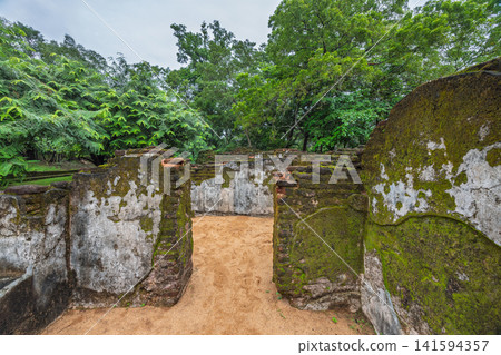 Ancient Royal Palace Ruins in Polonnaruwa, Sri Lanka. Ancient stone ruins covered in vibrant green moss within a lush, tropical forest setting under a cloudy sky Ancient Royal Palace Ruins in Polonnaruwa, Sri Lanka. Ancient stone ruins covered in vibrant green moss within a lush, tropical forest setting under a cloudy sky 141594357