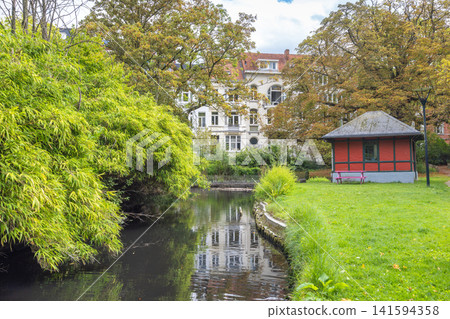 Ghent town in Belgium, Europe. Tranquil Urban Waterway with Historic Architecture and Lush Greenery Reflect in Calm Waters on an Overcast Day Ghent town in Belgium, Europe. Tranquil Urban Waterway with Historic Architecture and Lush Greenery Reflect in Calm Waters on an Overcast Day 141594358