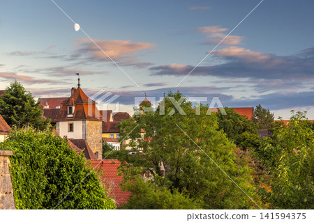 Rothenburg ob der Tauber, medieval old town in region of Bavaria in Germany, Europe. Historic Old Town View with Moon and Traditional Red Roofs Against Evening Sky Rothenburg ob der Tauber, medieval old town in region of Bavaria in Germany, Europe. Historic Old Town View with Moon and Traditional Red Roofs Against Evening Sky 141594375
