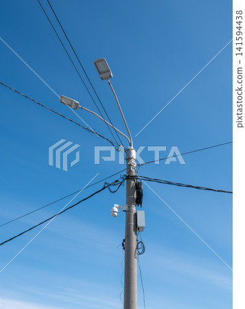 Street pole with lights junction box surveillance camera and cables against blue sky urban infrastructure security system. Street pole with lights junction box surveillance camera and cables against blue sky urban infrastructure security system. 141594438