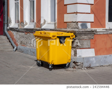 Yellow waste container on street corner near residential building urban sanitation concept. Yellow waste container on street corner near residential building urban sanitation concept. 141594446