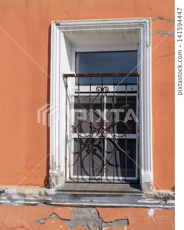 Window with decorative wrought iron grille architectural detail on building facade. 141594447