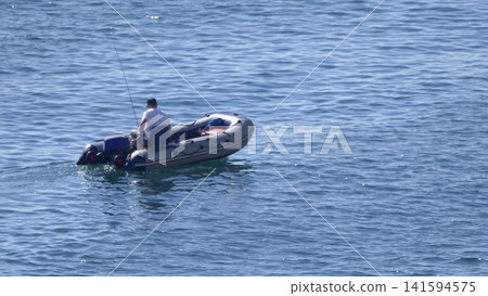 A fisherman in an inflatable boat on the sea. Calm water, clear sky, peaceful maritime scene A fisherman in an inflatable boat on the sea. Calm water, clear sky, peaceful maritime scene 141594575