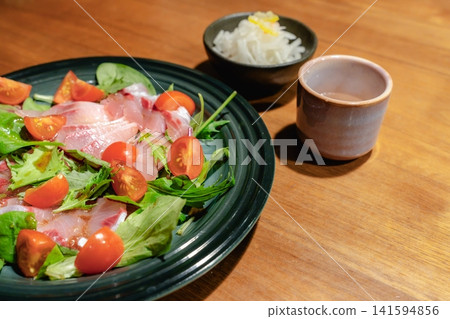 A scene from a dinner table featuring fresh fish carpaccio and side dishes. 141594856