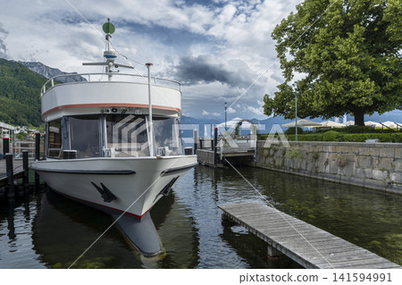 Passenger boat docked at a wooden pier on Lake Traunsee with an alpine mountain landscape, illustrating summer tourism in Austria. Passenger boat docked at a wooden pier on Lake Traunsee with an alpine mountain landscape, illustrating summer tourism in Austria. 141594991