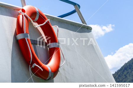 Orange lifebuoy on a boat illustrates maritime safety and essential emergency preparedness in waterfront environments. Orange lifebuoy on a boat illustrates maritime safety and essential emergency preparedness in waterfront environments. 141595017