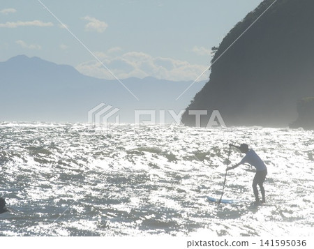 一位遊客在湘南地區享受立式槳板衝浪，欣賞波光粼粼的大海。 141595036