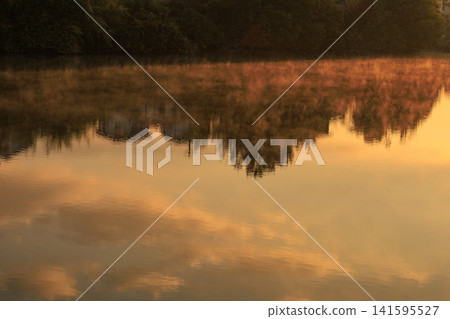 Late autumn scenery at a reservoir: sea fog drifts across the lake's surface, reflecting the morning glow. Late autumn scenery at a reservoir: sea fog drifts across the lake's surface, reflecting the morning glow. 141595527