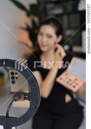 Asian woman filming beauty vlog tutorial with ring light, reviewing cosmetics and makeup concept. Asian woman filming beauty vlog tutorial with ring light, reviewing cosmetics and makeup concept. 141595587