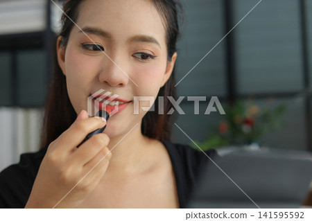 Beautiful Asian woman putting on makeup cosmetic at home. Beautiful Asian woman putting on makeup cosmetic at home. 141595592