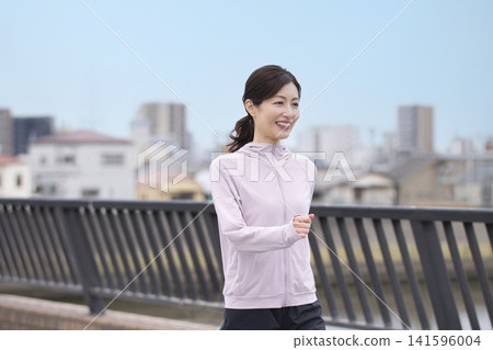 一位中年婦女身穿運動服沿著河岸行走。 141596004