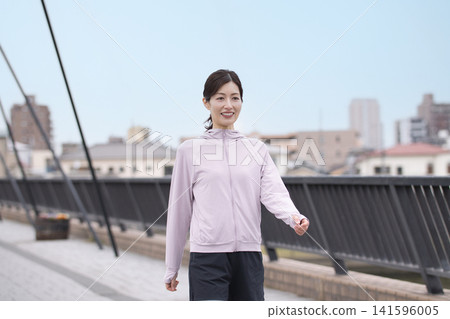 一位中年婦女身穿運動服沿著河岸行走。 一位中年婦女身穿運動服沿著河岸行走。 141596005