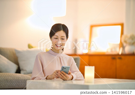 一位四十多歲的女性晚上在房間裡放鬆,看著她的智慧型手機。 一位四十多歲的女性晚上在房間裡放鬆,看著她的智慧型手機。 141596017