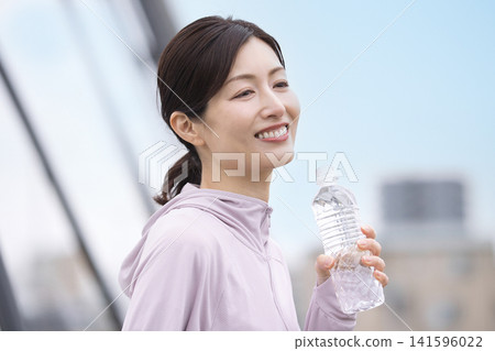 A middle-aged woman drinking bottled water while walking. A middle-aged woman drinking bottled water while walking. 141596022