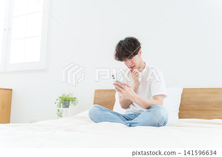 A young man using his smartphone while looking troubled. A young man using his smartphone while looking troubled. 141596634