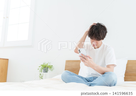 A young man using his smartphone while looking troubled. A young man using his smartphone while looking troubled. 141596635