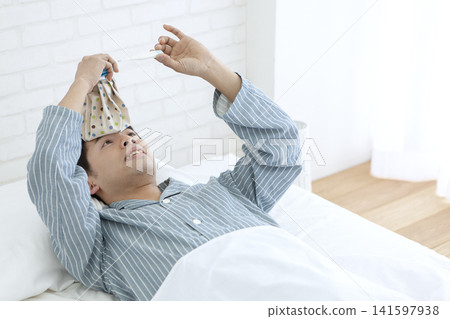 一名男子穿著睡衣在床上量體溫。 141597938