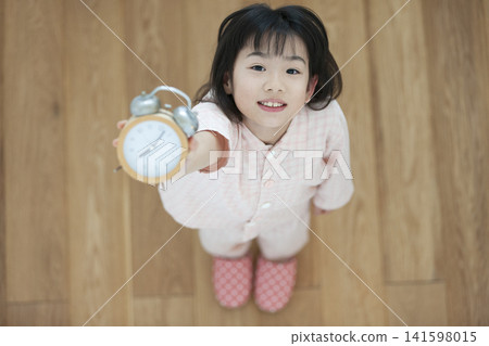 一個穿著睡衣的女孩拿著鬧鐘 141598015